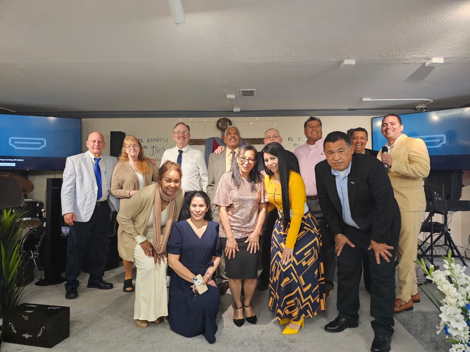 Grupo de personas en vestimenta formal posando juntas en un salón con carteles religiosos.